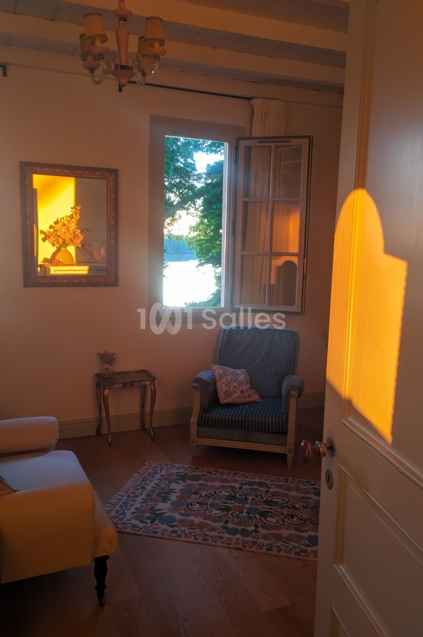 Salon chaleureux avec fauteuil, tapis et lumière dorée du soleil couchant entrant par une fenêtre ouverte.