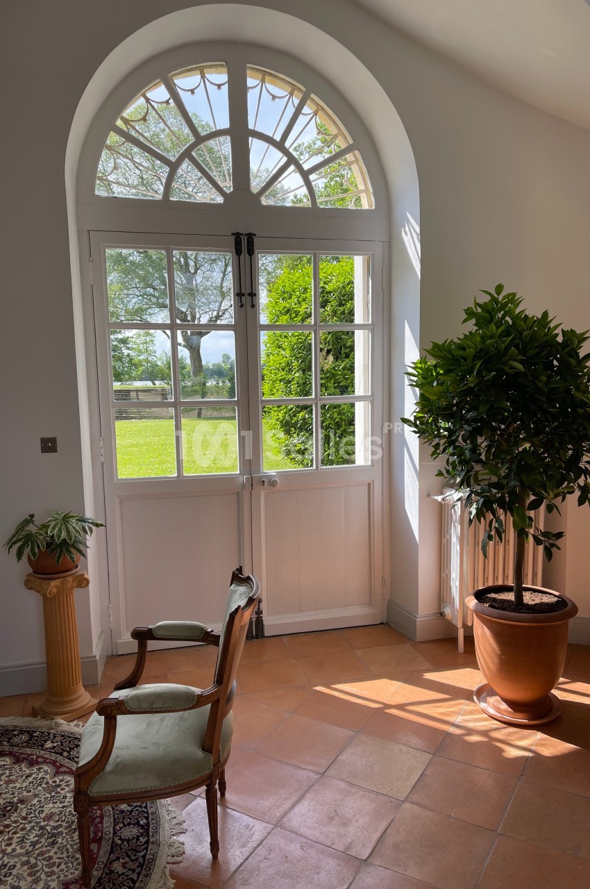 Porte-fenêtre cintrée donnant sur un jardin, éclairant une pièce avec fauteuils, tapis et plantes en pot.