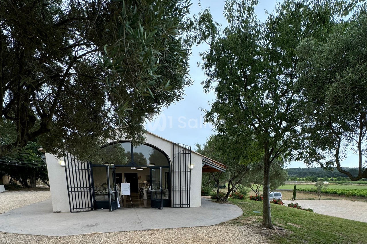 Bâtiment avec façade vitrée entouré d'arbres, situé dans un paysage rural avec des vignes en arrière-plan.
