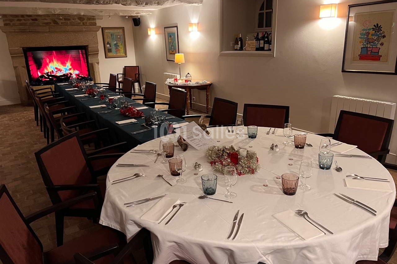Salle à manger décorée pour un repas festif, avec une grande table ronde et une cheminée virtuelle allumée.