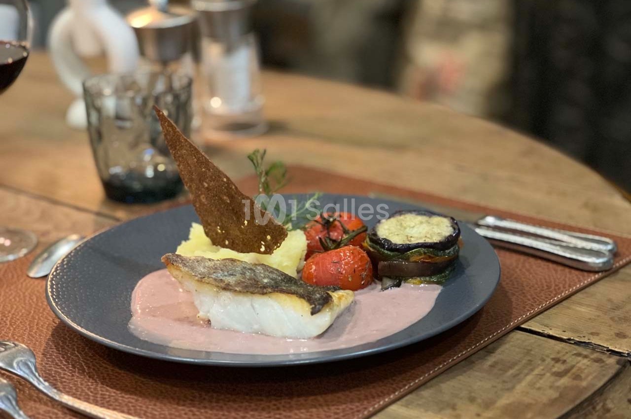 Assiette de poisson accompagné de purée, légumes grillés et sauce, servie sur une table en bois.