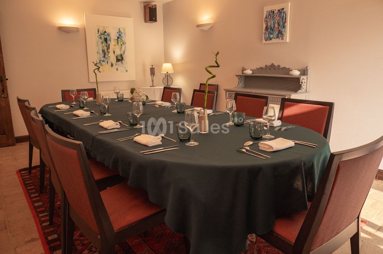 Salle à manger élégante avec une grande table ovale dressée, entourée de chaises rouges, éclairée par des lampes.