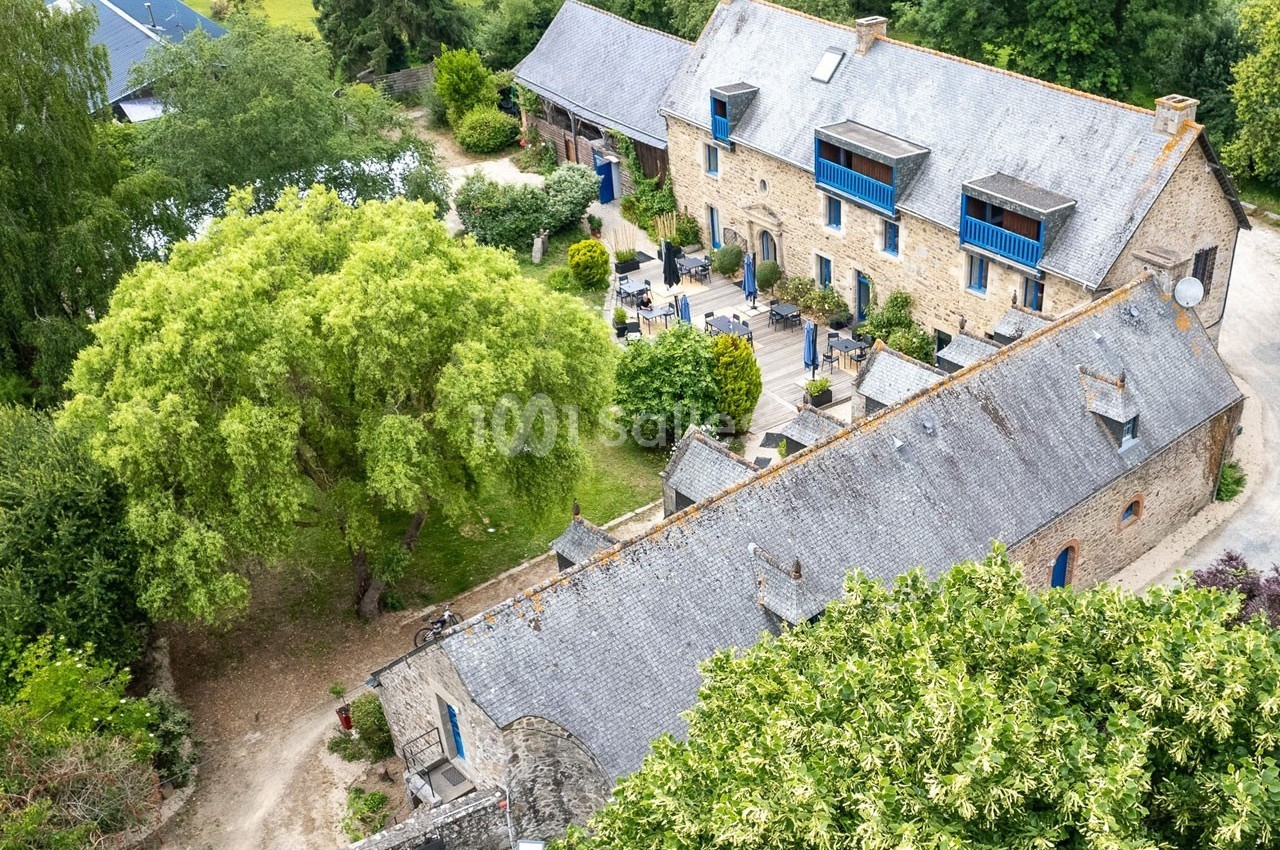 Vue aérienne d'un ensemble de bâtiments en pierre avec toits en ardoise, entouré de verdure et d'arbres.