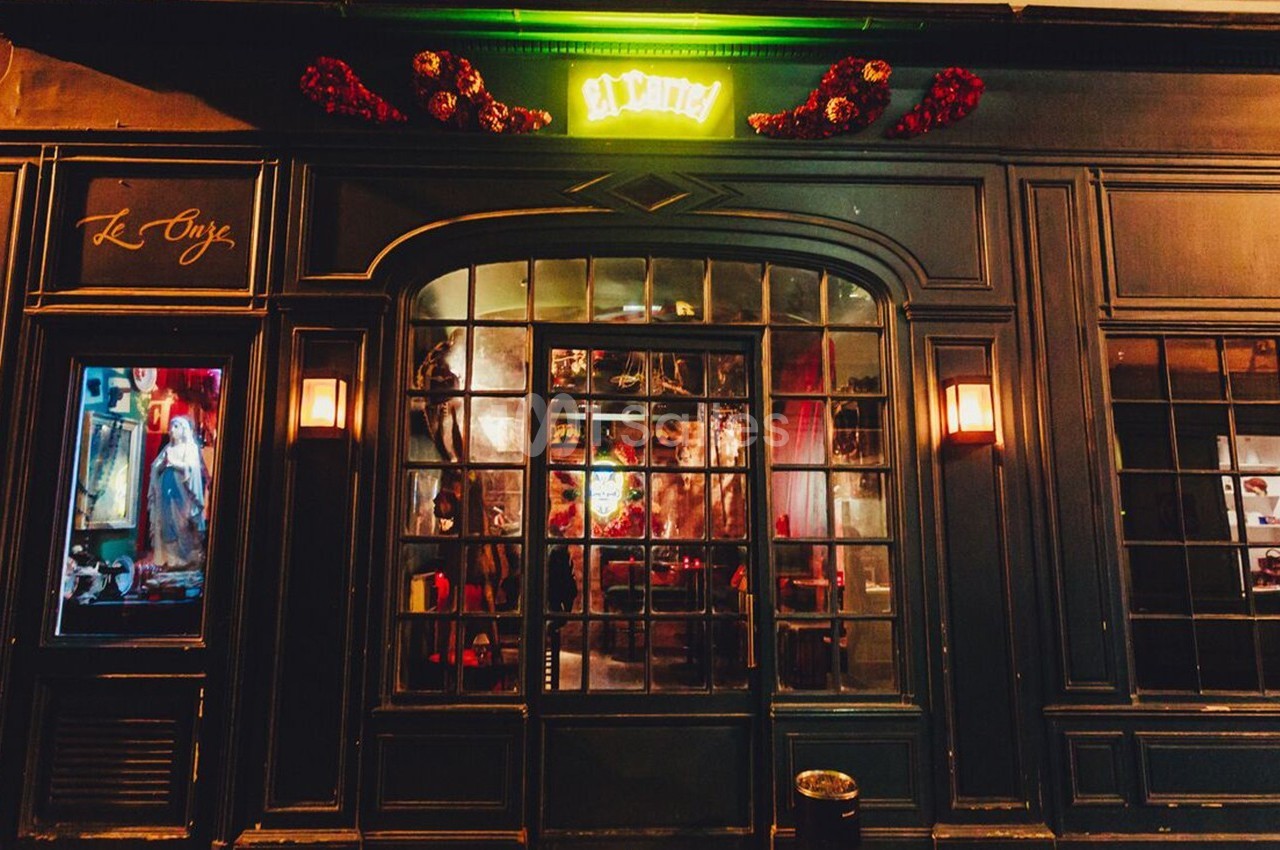 Façade d'une boutique avec vitrine éclairée, enseigne lumineuse verte et décoration florale rouge au-dessus.