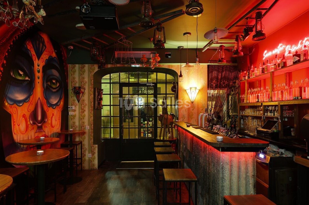 Bar à l'ambiance tamisée avec un mur décoré d'une fresque colorée et un éclairage rouge néon au-dessus du comptoir.