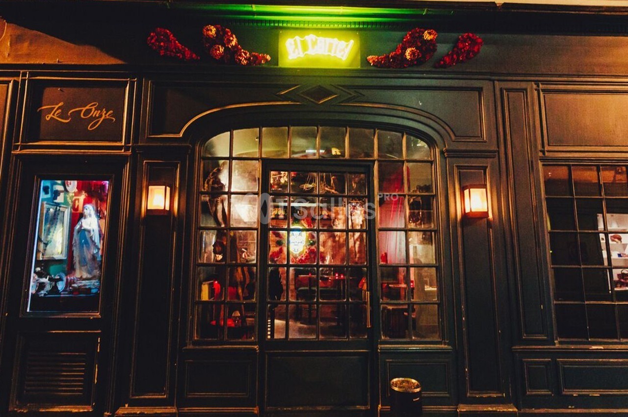Façade d'une boutique avec une devanture vitrée, éclairée par des lumières chaudes et une enseigne lumineuse verte.
