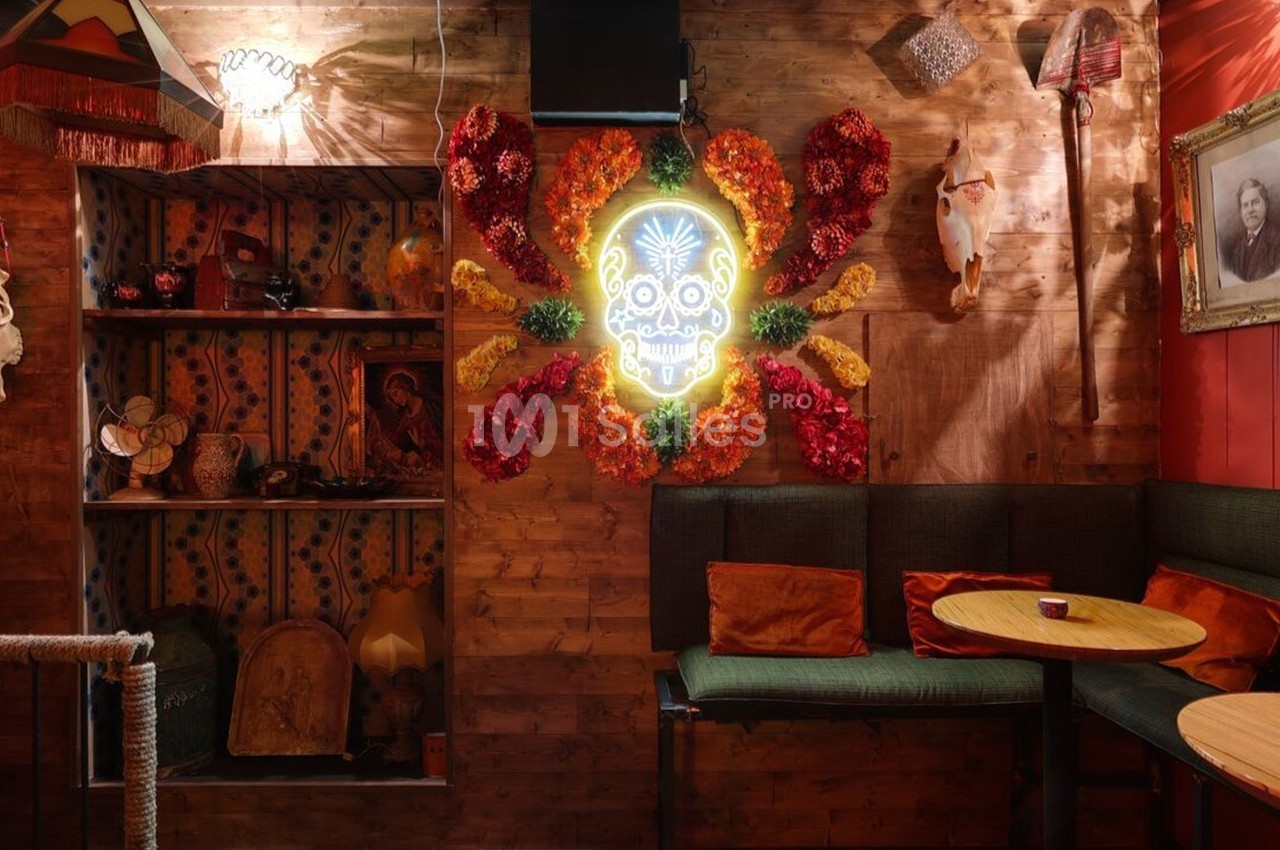 Décoration intérieure colorée avec mur en bois, néon en forme de crâne entouré de fleurs, et coin salon avec tables.