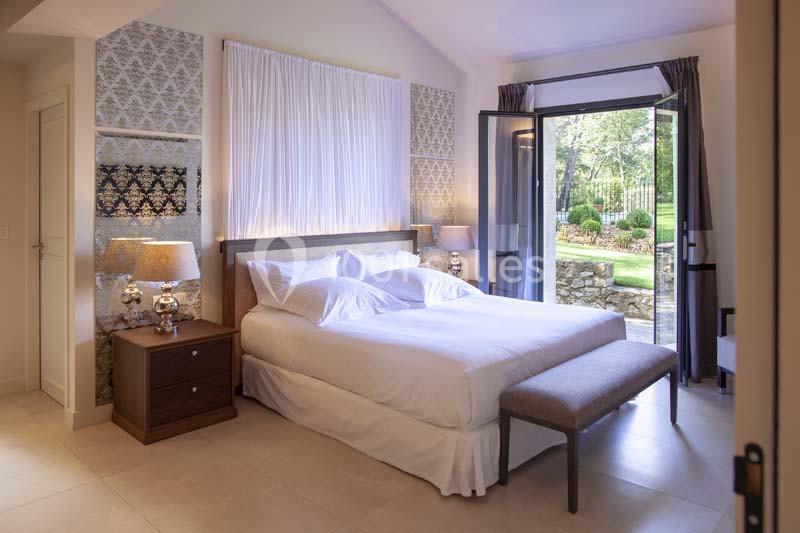 Chambre lumineuse avec lit double, lampes de chevet, rideaux ouverts donnant sur un jardin verdoyant.