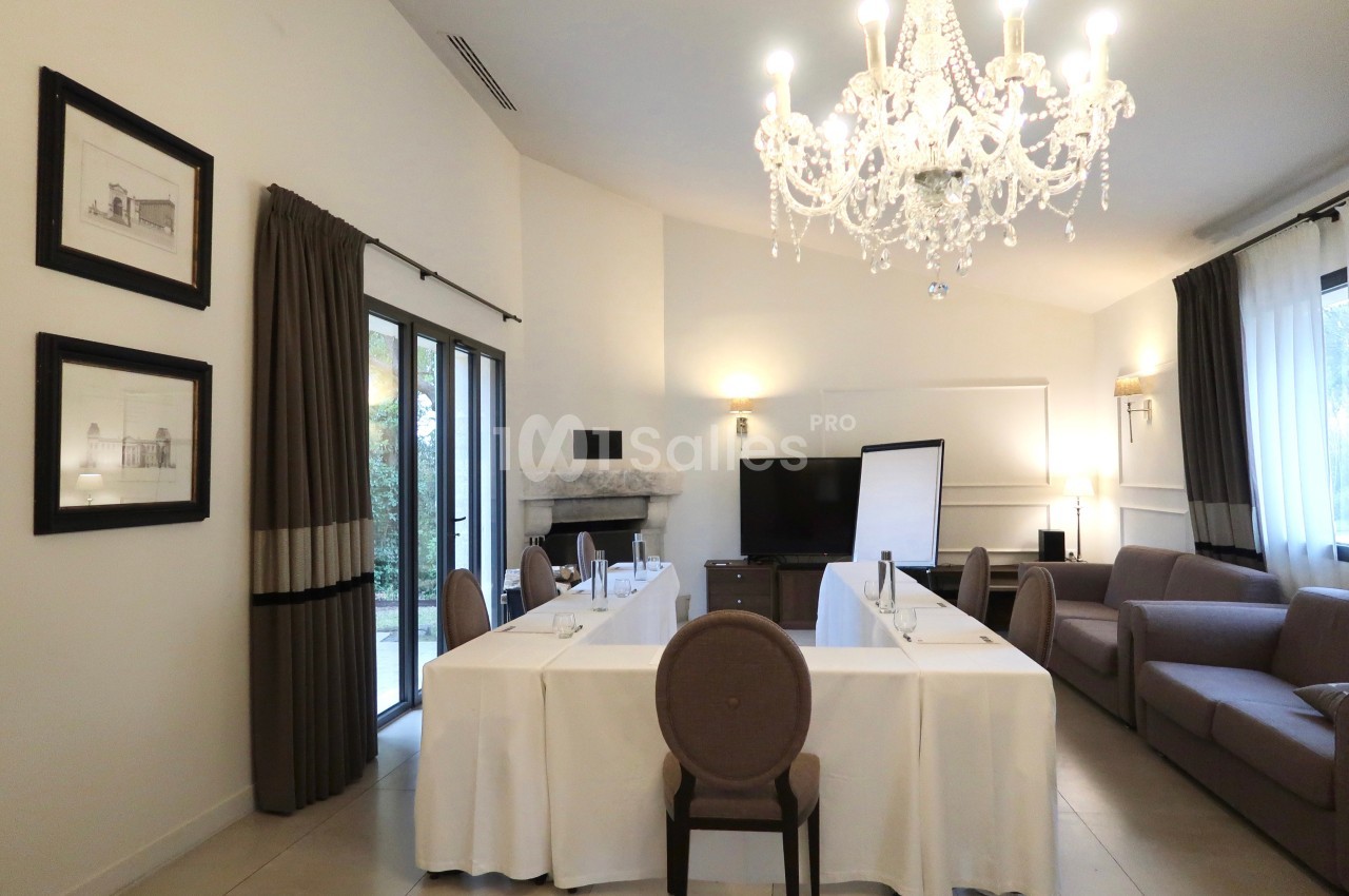 Salle de réunion lumineuse avec tables dressées, chaises, un tableau blanc, un canapé et un lustre élégant.