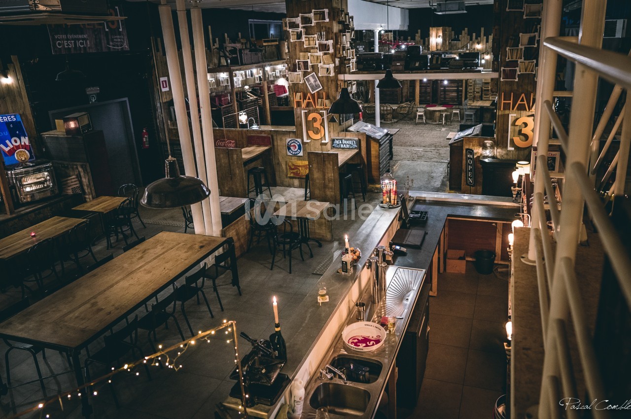 Vue d'un espace intérieur industriel avec tables en bois, comptoir, éclairage tamisé et décoration vintage.
