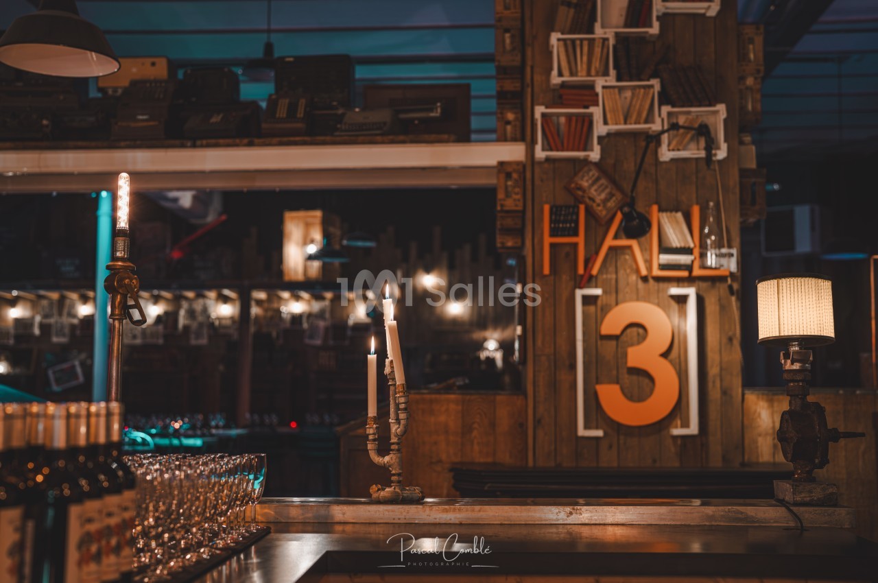 Intérieur d'un bar avec des bougies allumées, des étagères décoratives et un panneau indiquant ’Hall 3’.