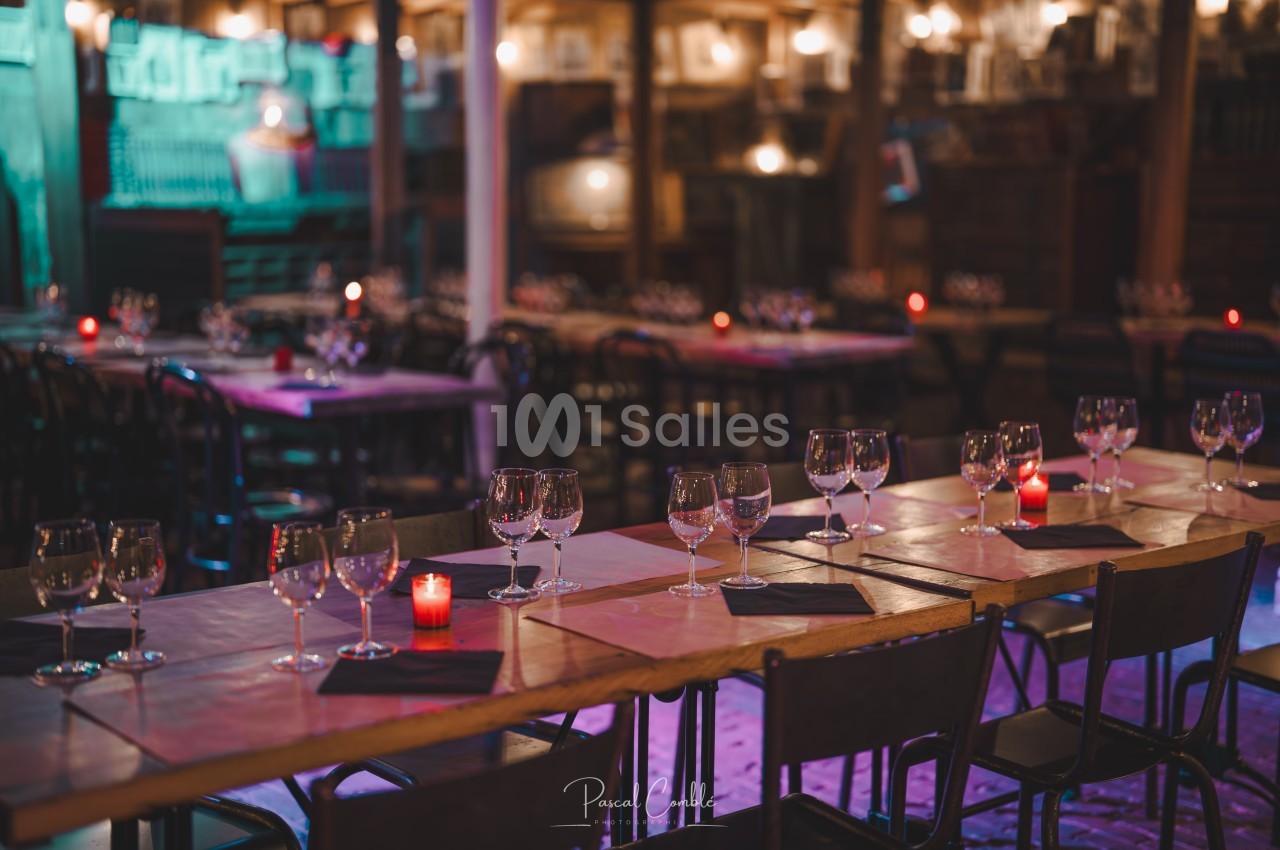 Salle de restaurant avec tables en bois dressées, verres à vin et bougies rouges allumées dans une ambiance tamisée.