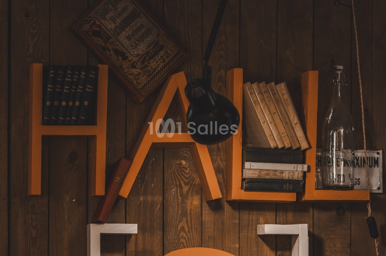 Étagère murale en bois avec des lettres orange formant ’HAL’, décorée de livres, d'une lampe et d'une bouteille en verre.