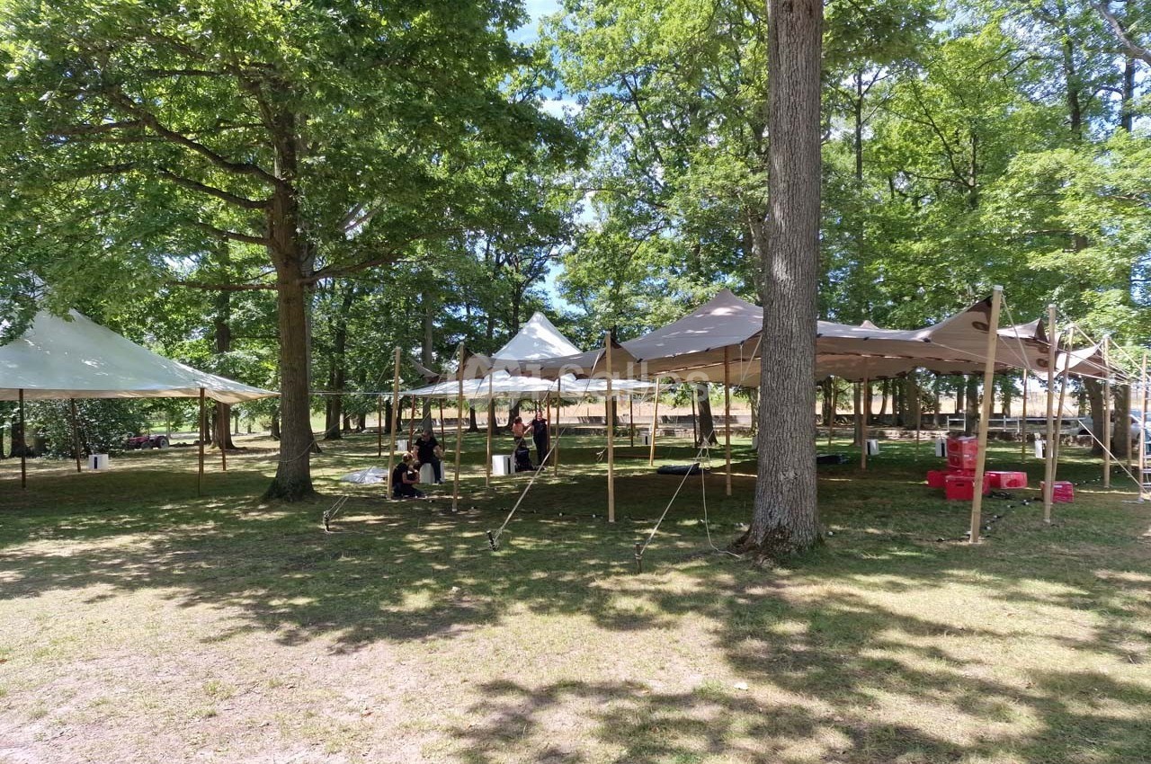 Tentes installées dans une clairière ombragée avec quelques personnes assises sous l'une d'elles.