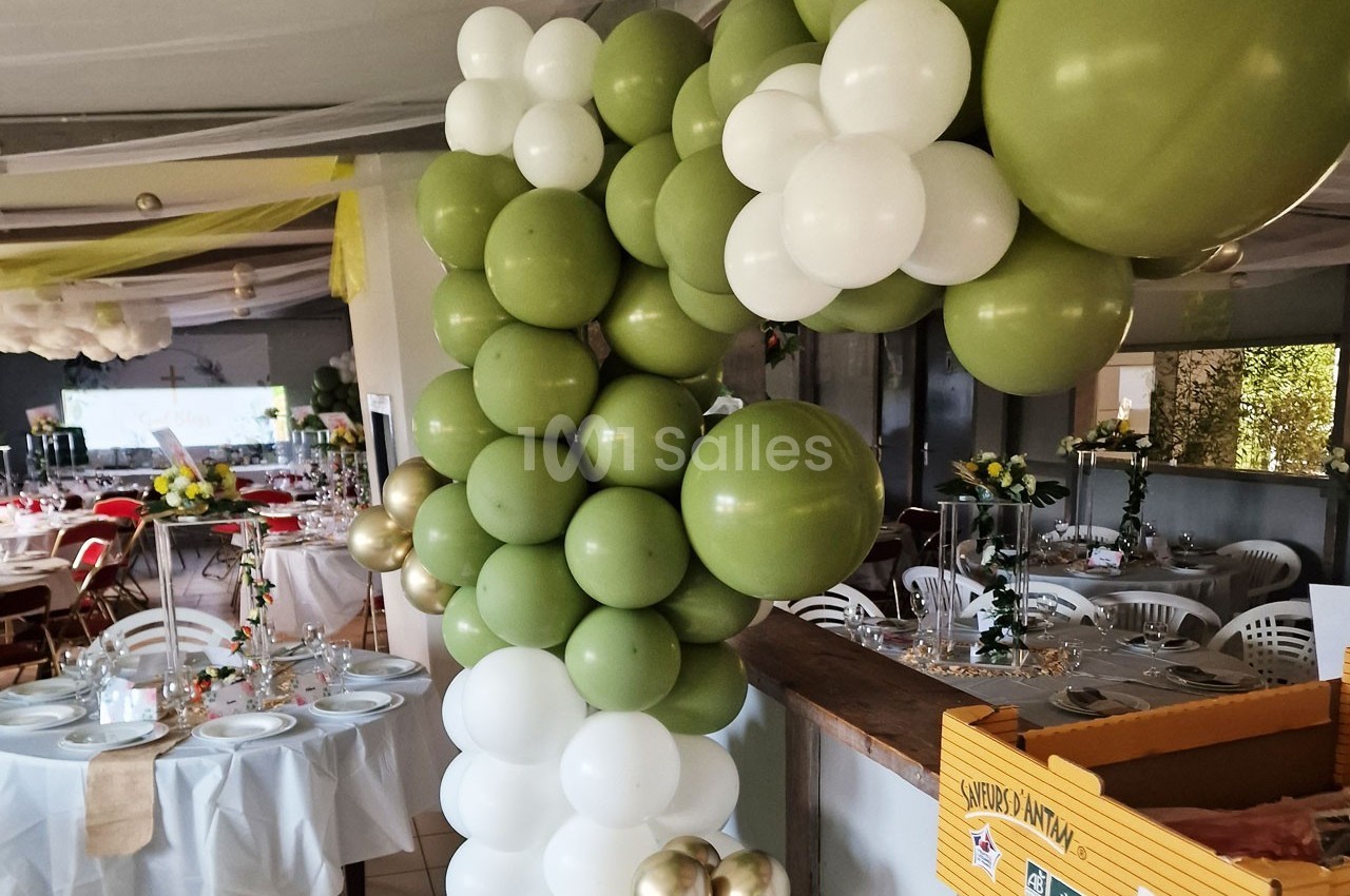 Décoration de salle avec arche de ballons verts et blancs, tables dressées pour un événement festif.
