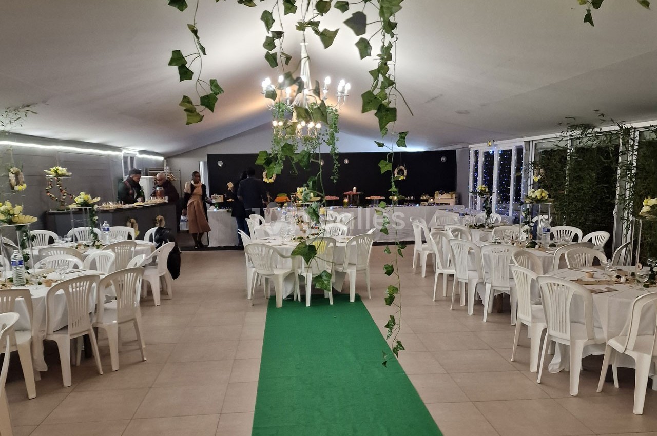 Salle de réception décorée avec des plantes suspendues, tables dressées et buffet au fond.