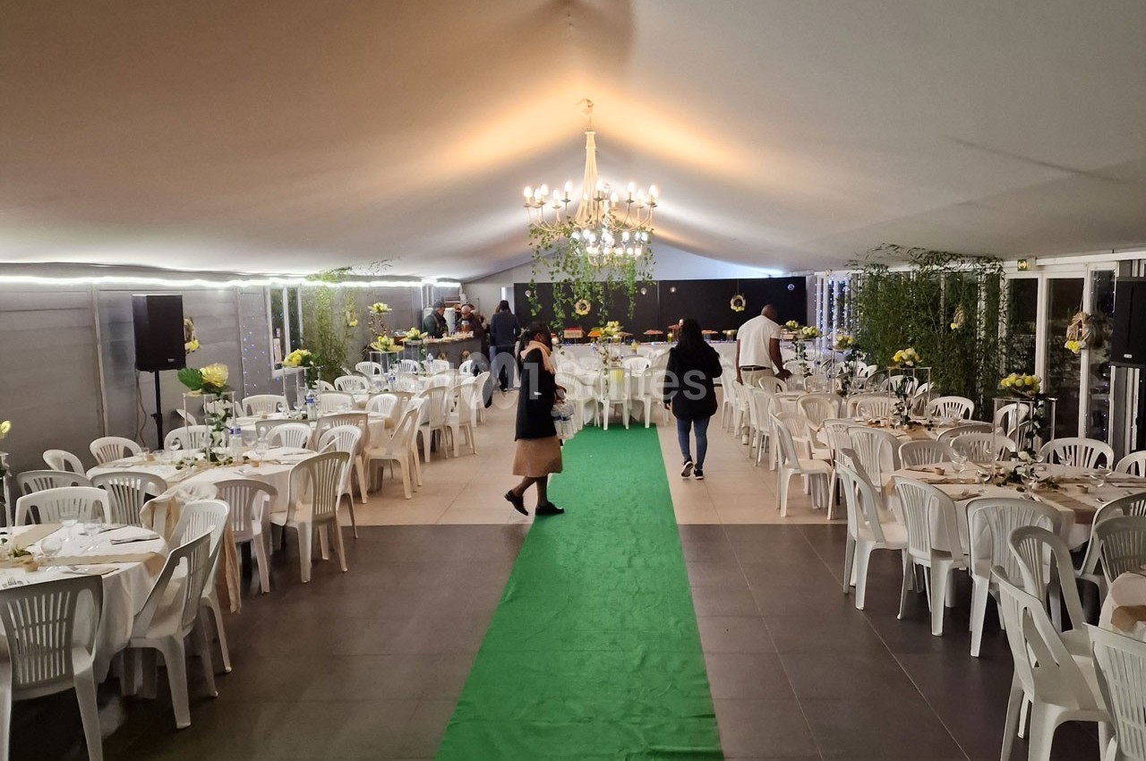 Salle de réception décorée avec des tables blanches, un tapis vert central et un lustre suspendu.