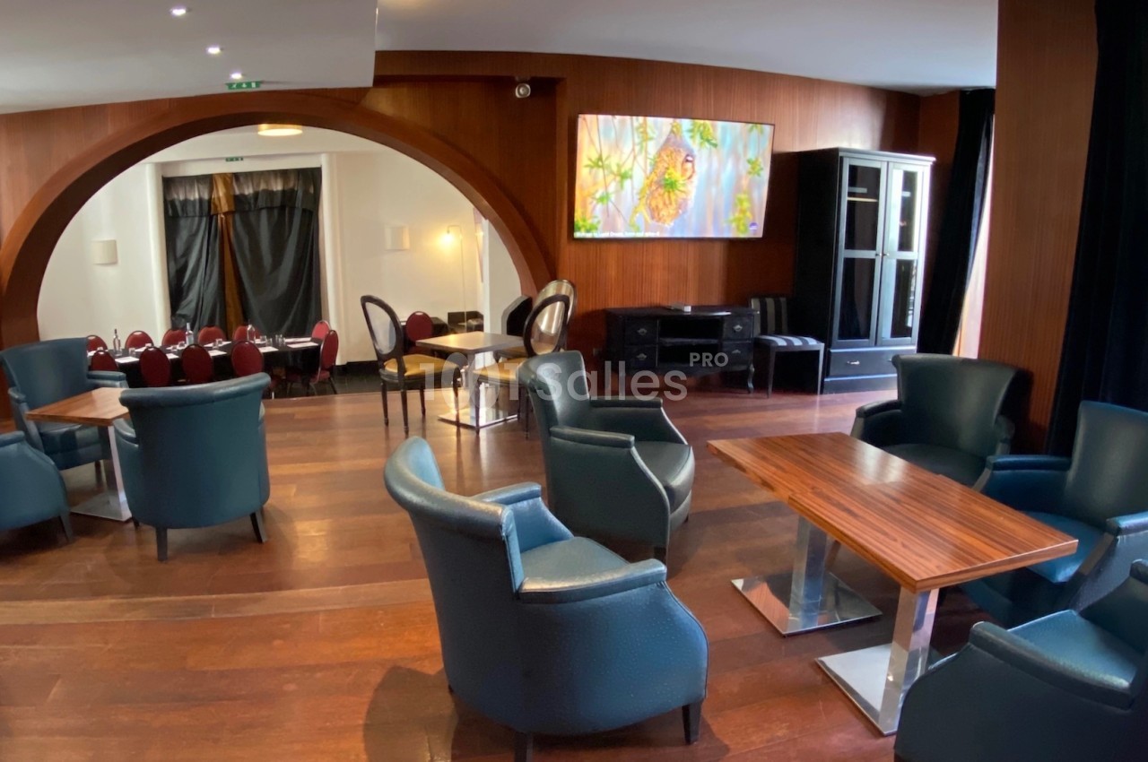 Salle avec fauteuils en cuir, tables en bois, grande arche, tableau coloré et lumière naturelle provenant d'une baie vitrée.