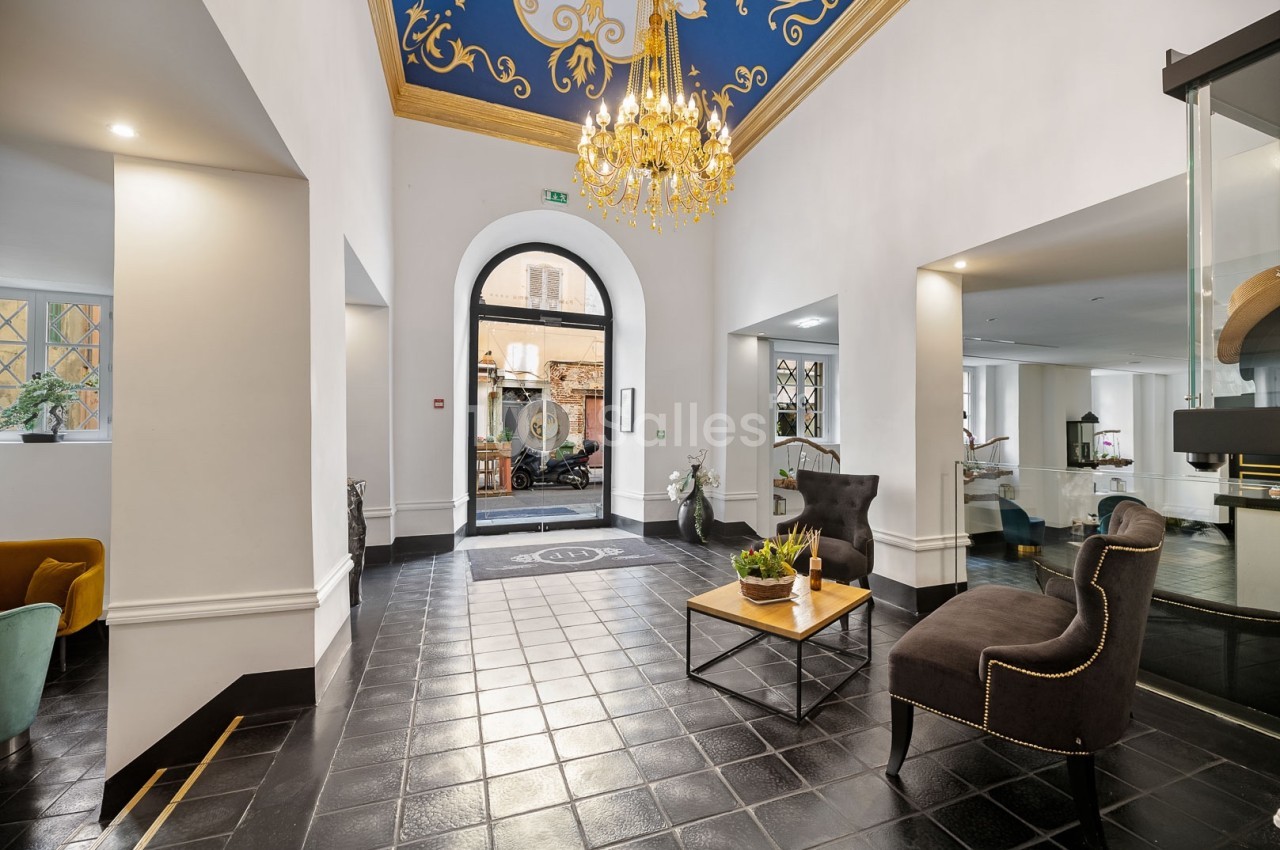 Hall d'entrée lumineux avec sol en carrelage noir, plafond décoré, lustre doré et mobilier élégant.