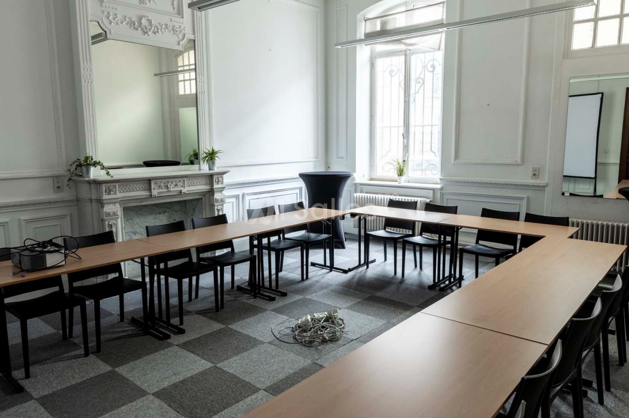 Salle de réunion lumineuse avec des tables disposées en U, des chaises noires et un amas de câbles au sol.