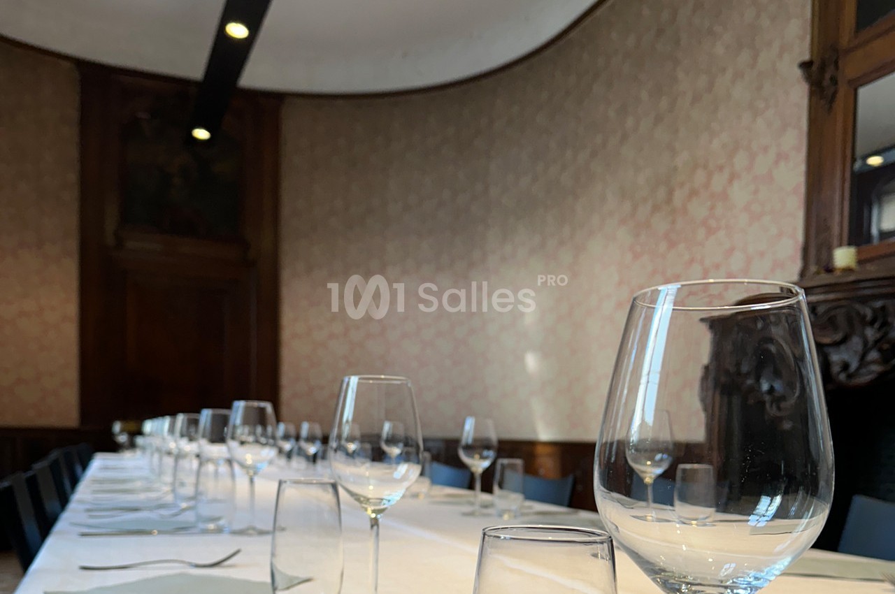 Table dressée avec nappes blanches, verres et serviettes, dans une salle élégante aux murs ornés et boiseries.