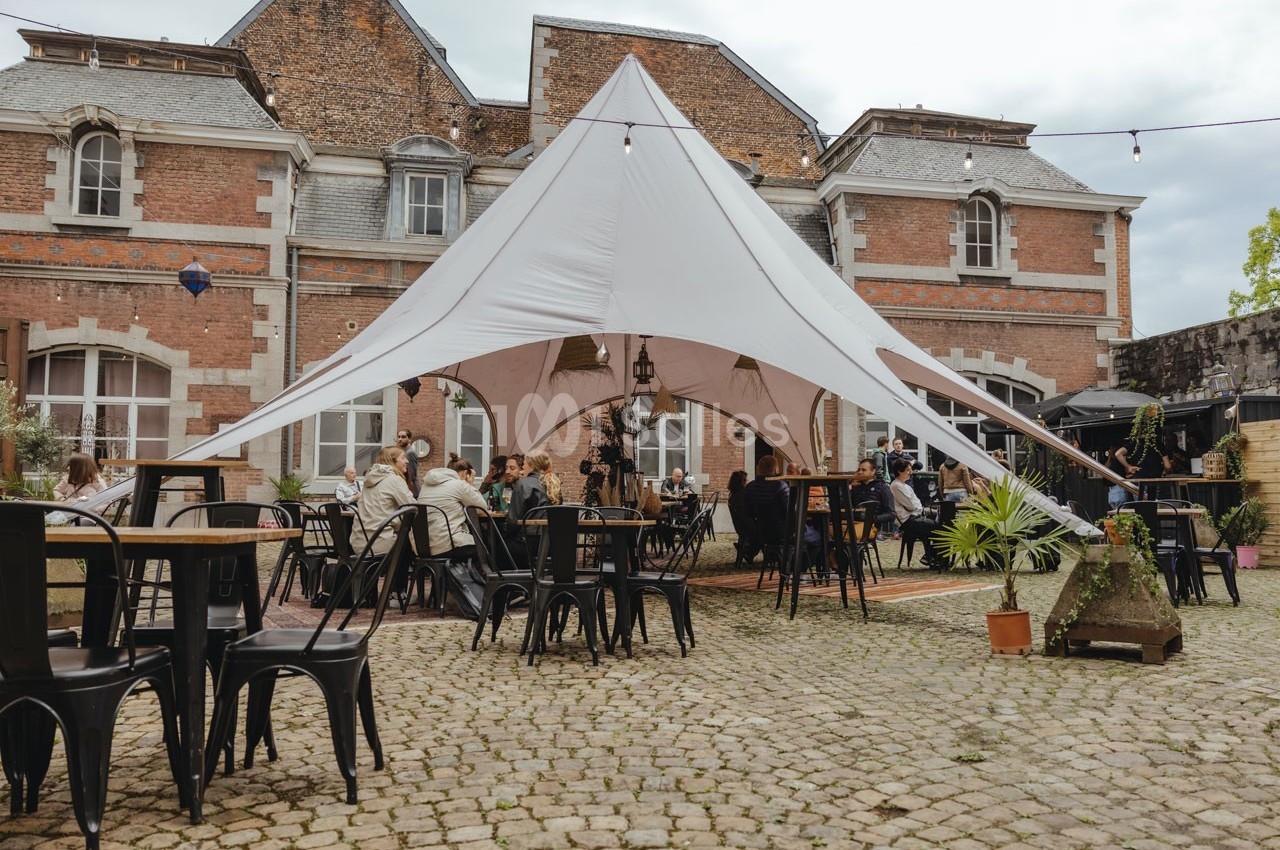 Cour extérieure pavée avec une grande tente blanche, des tables et des chaises, et des personnes attablées.
