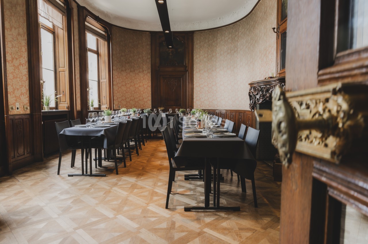Salle élégante avec tables dressées, chaises noires et grandes fenêtres laissant entrer la lumière naturelle.