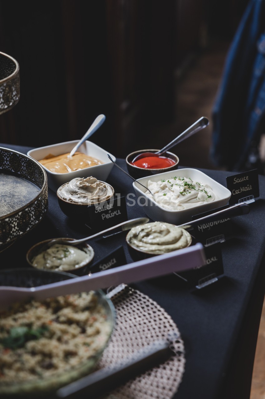 Assortiment de sauces variées dans des bols avec étiquettes, disposées sur une table sombre.