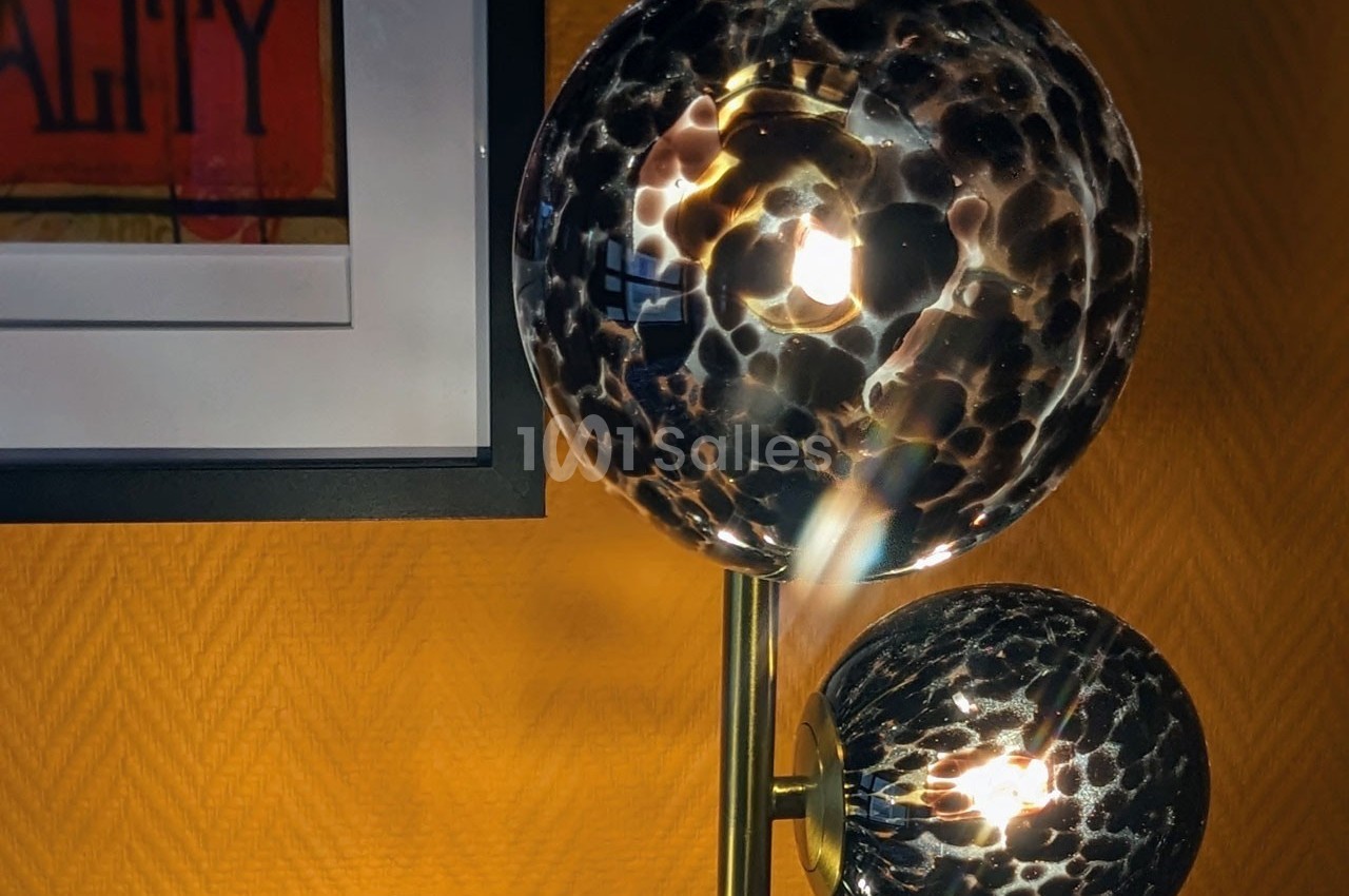Lampe à globes en verre texturé noir et doré, allumée, devant un mur jaune avec un cadre accroché.
