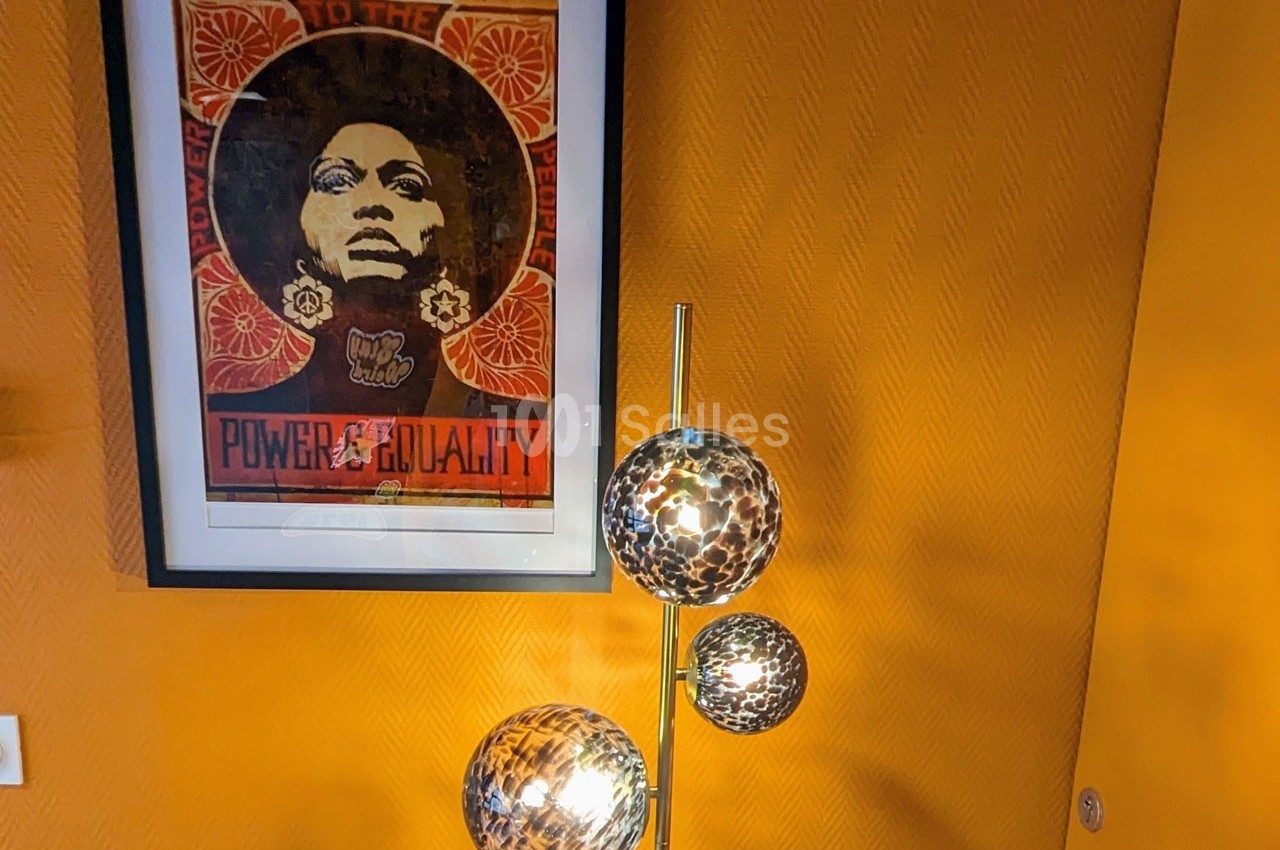 Affiche encadrée sur un mur jaune avec une lampe à trois globes lumineux au premier plan.