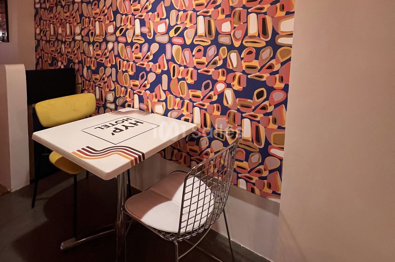Table et deux chaises dans un coin de pièce avec un mur décoré d'un papier peint coloré à motifs géométriques.