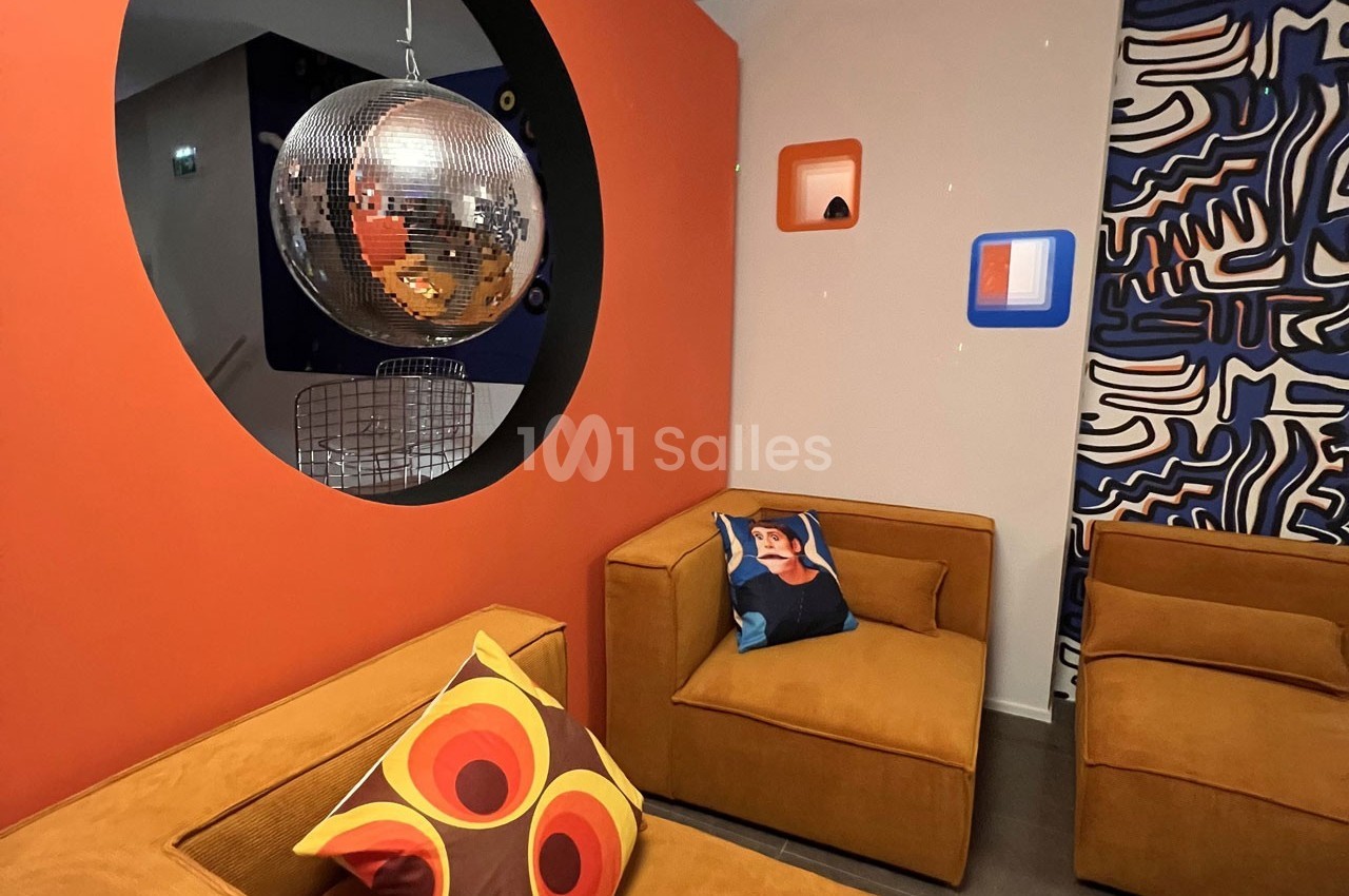 Salon moderne avec fauteuils en velours orange, coussins colorés, boule à facettes et décoration murale graphique.