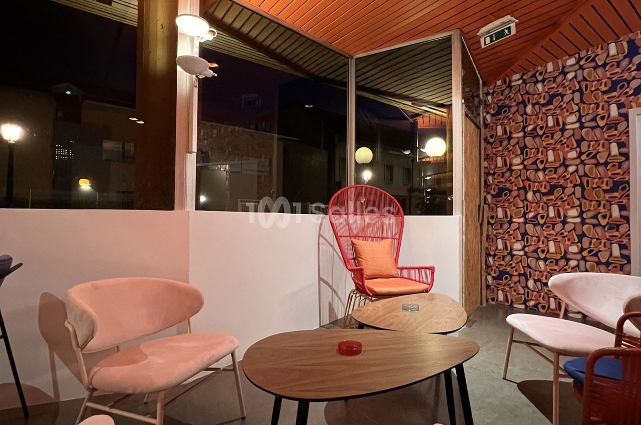 Espace intérieur avec mobilier coloré, chaises et tables, éclairé par des lampes et une grande baie vitrée donnant sur l…