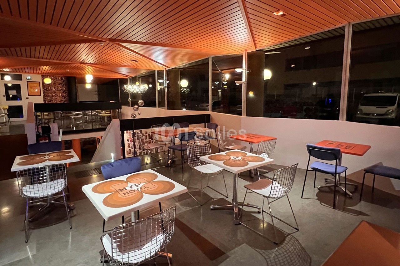 Salle de restaurant moderne avec tables décorées, chaises en métal et éclairage chaleureux.