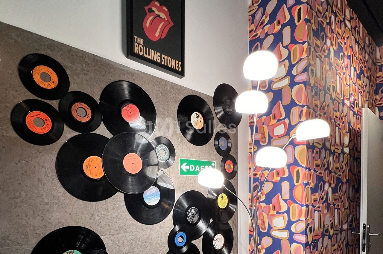 Mur décoré de vinyles, panneau des Rolling Stones et lampes modernes, avec un papier peint coloré en arrière-plan.