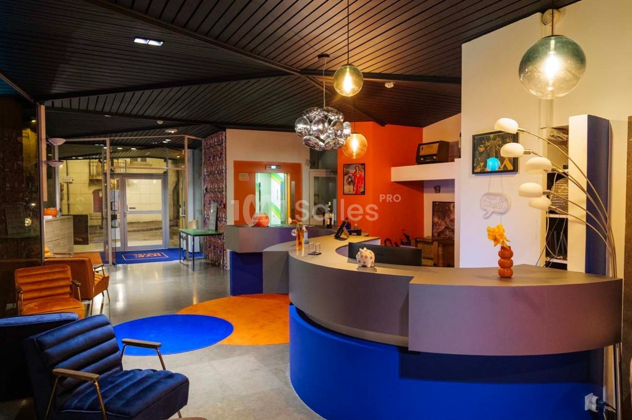 Intérieur d'un hall d'accueil moderne avec comptoir arrondi, fauteuils, décorations colorées et éclairage design.