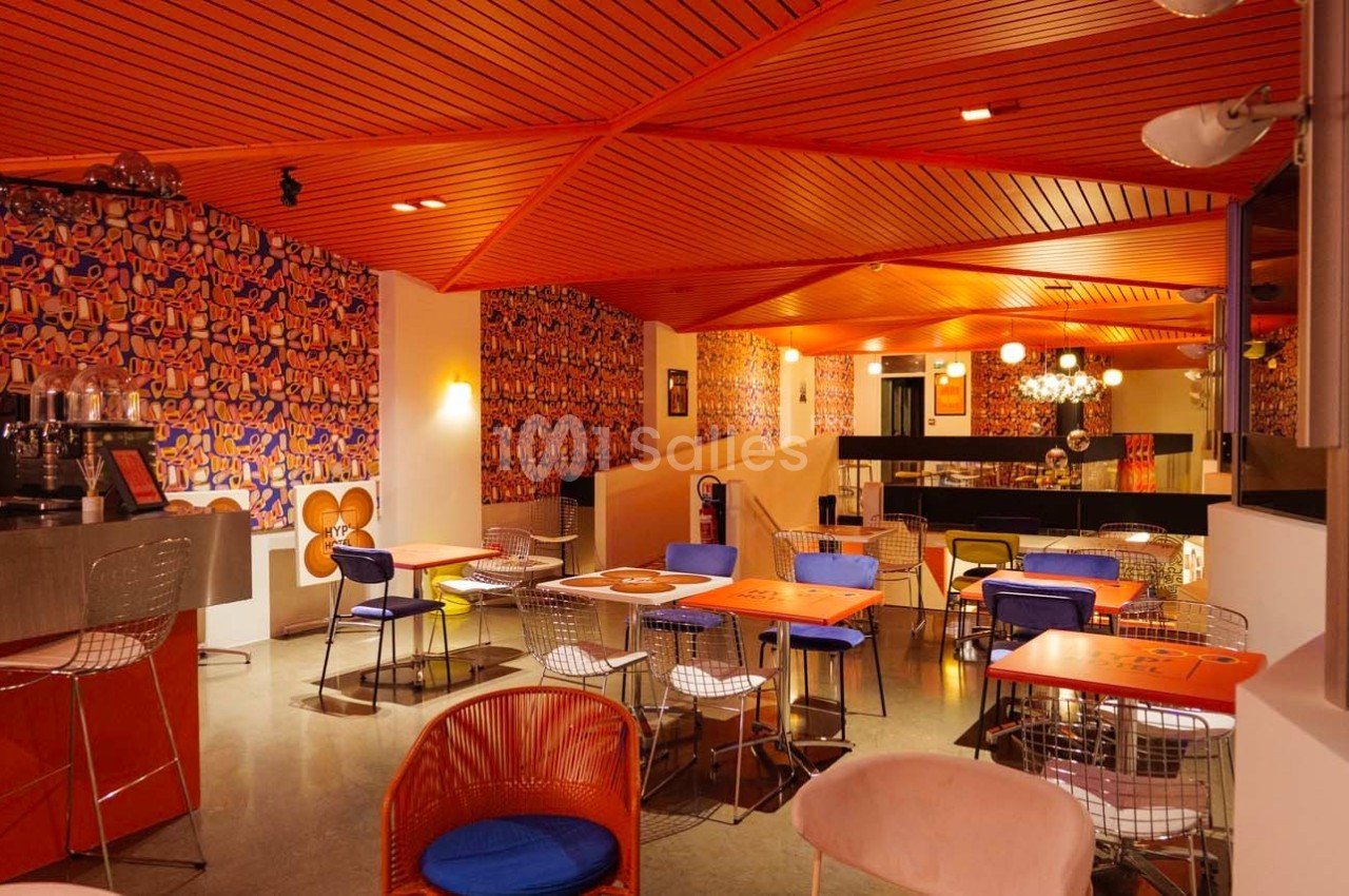 Salle de restaurant colorée avec des murs ornés de motifs vifs, des tables orange et des chaises modernes.