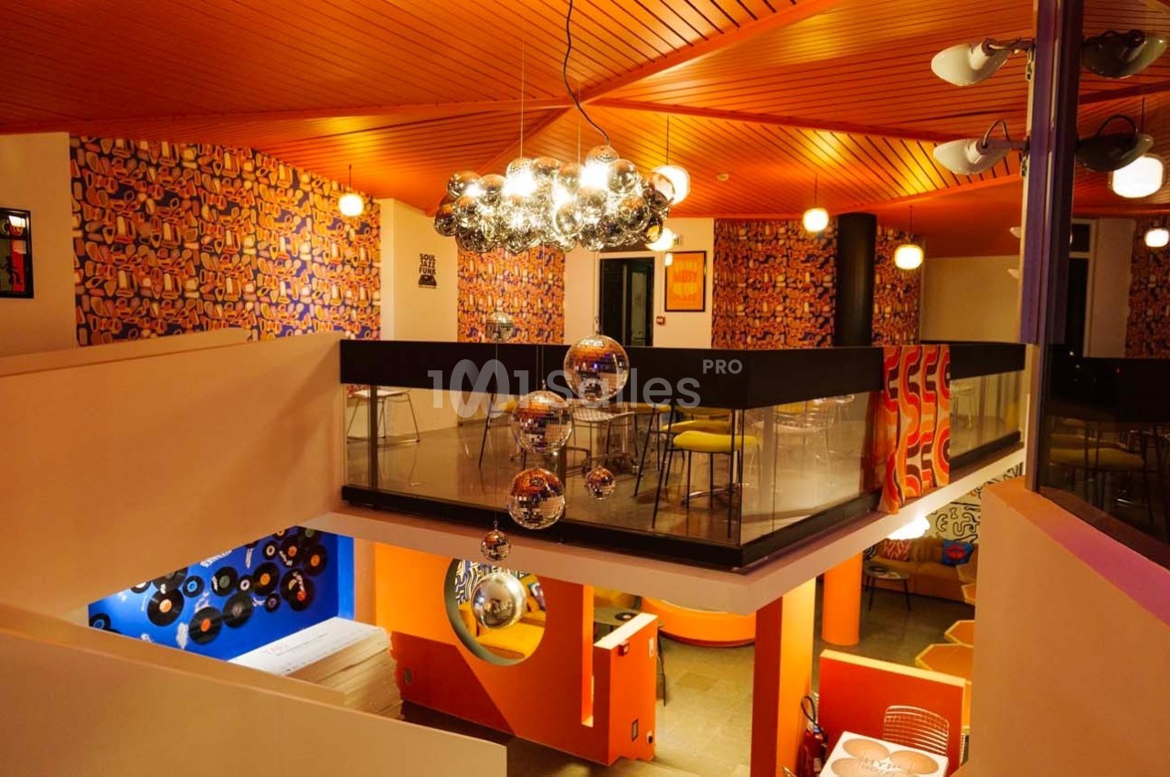Intérieur coloré avec mezzanine, murs décorés de motifs vifs, luminaires modernes et ambiance rétro.