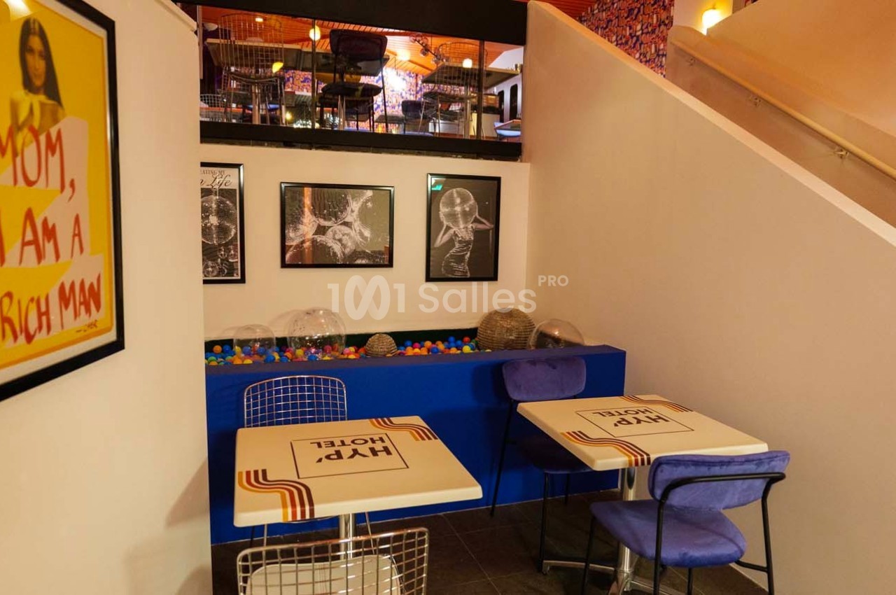 Deux tables avec chaises dans un café coloré, décoré de cadres, d'une affiche et d'une piscine à balles.