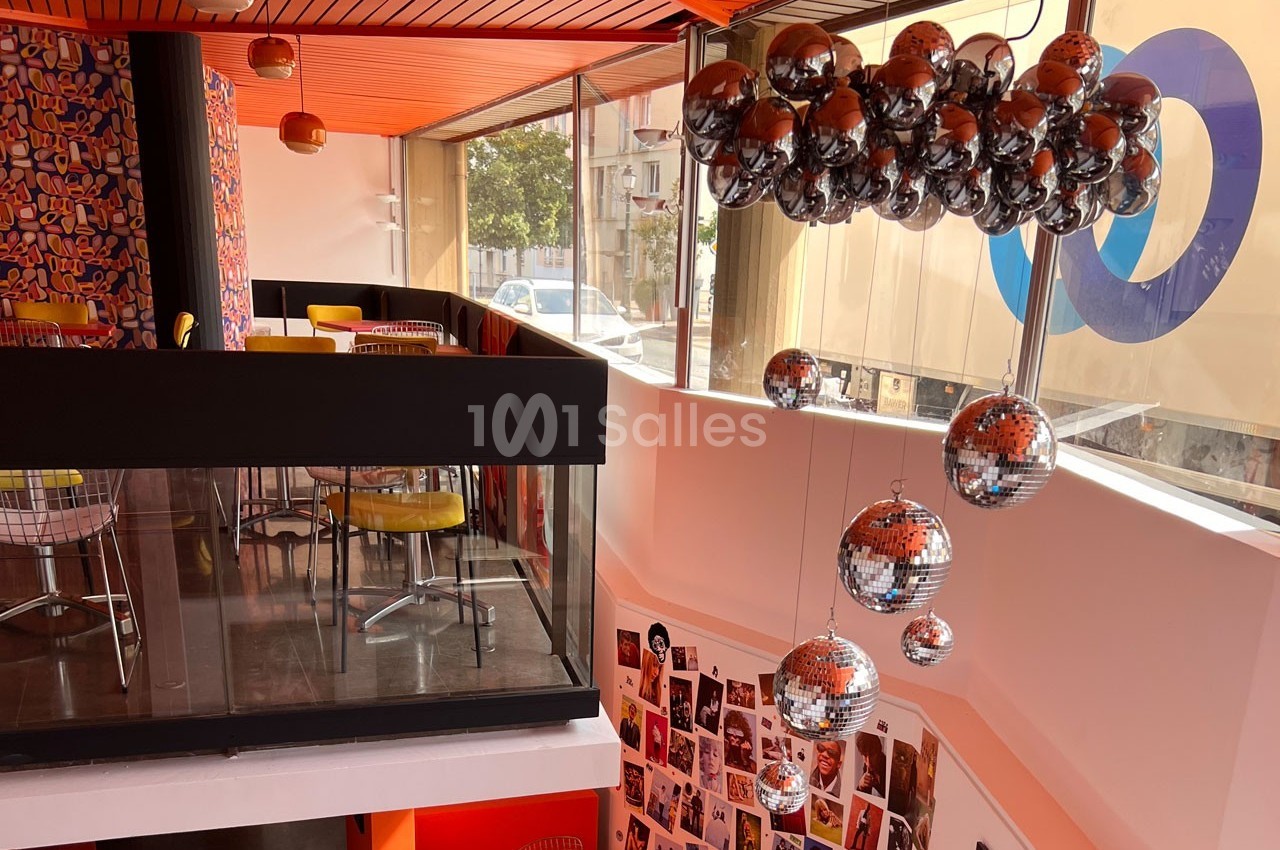 Intérieur coloré d'un café moderne avec mezzanine, chaises jaunes, murs décorés et lustre en boules miroir.