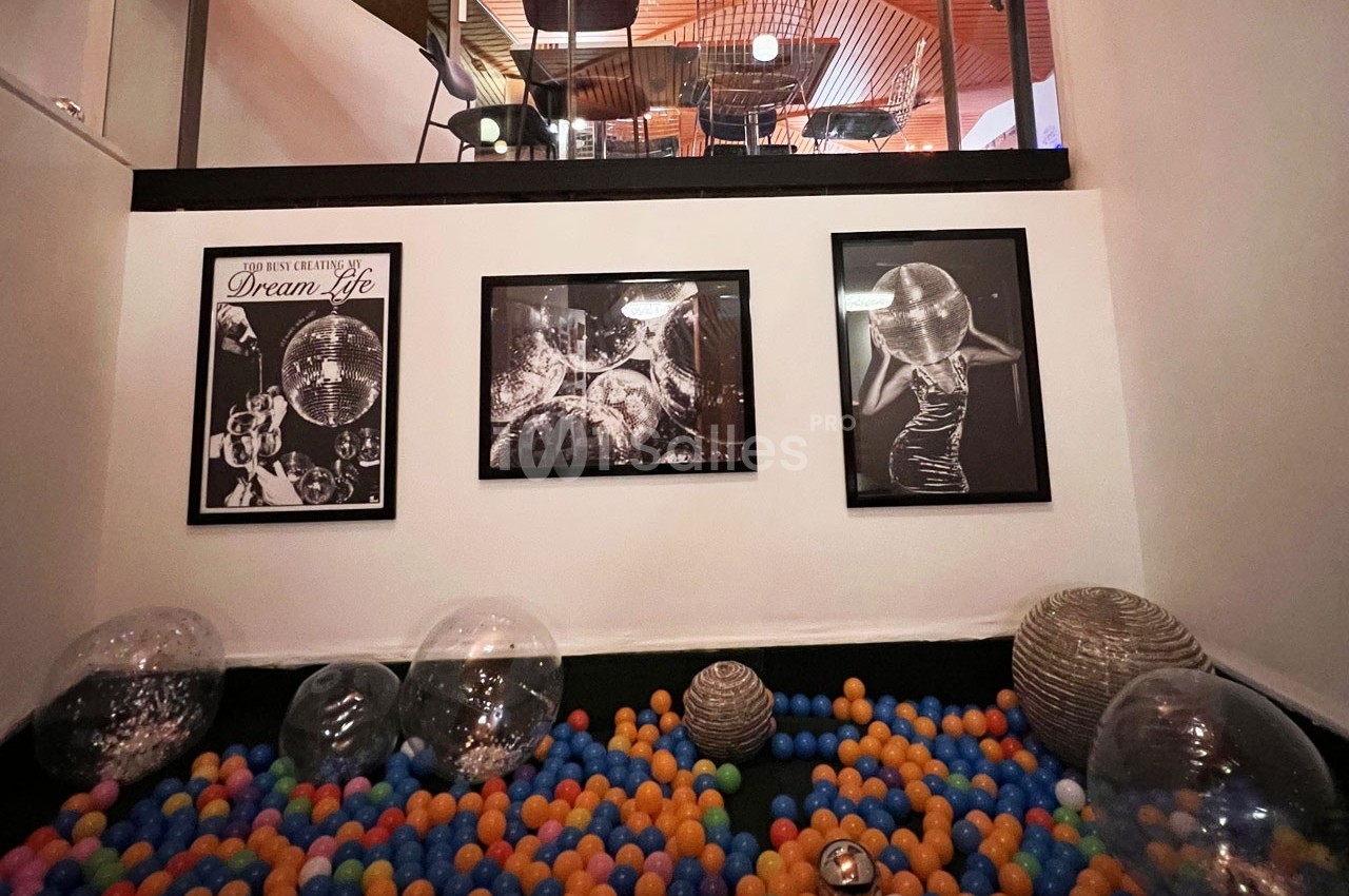 Piscine à balles colorées avec des ballons transparents, décorée de photos en noir et blanc sur un mur blanc.