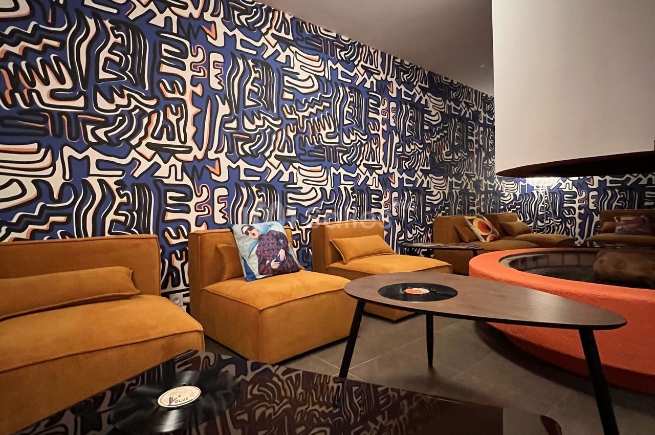 Salon avec fauteuils jaunes, table basse noire, mur décoré de motifs abstraits bleus et blancs, ambiance chaleureuse.