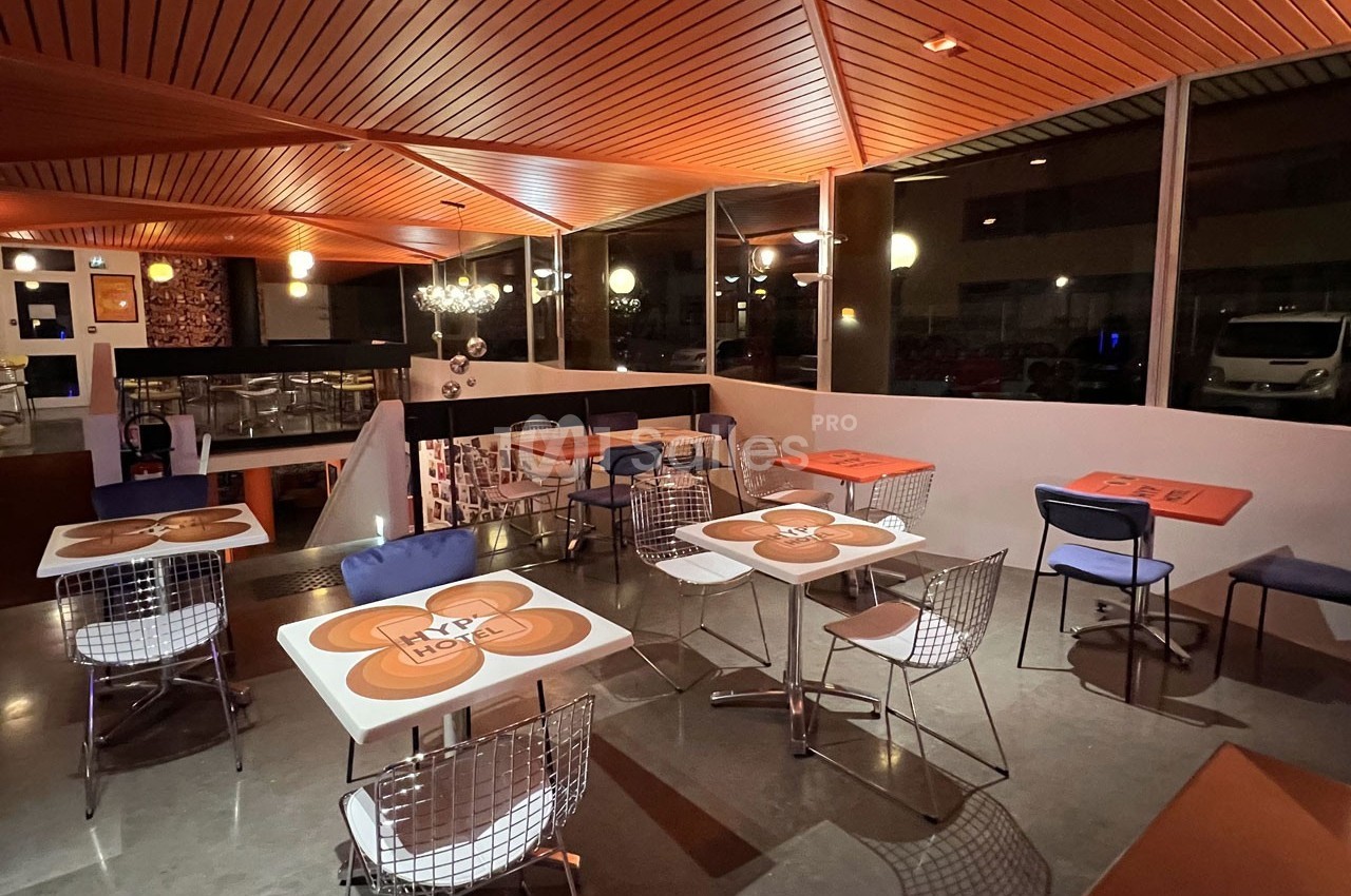 Salle de restaurant moderne avec tables décorées, chaises en métal et éclairage chaleureux en soirée.