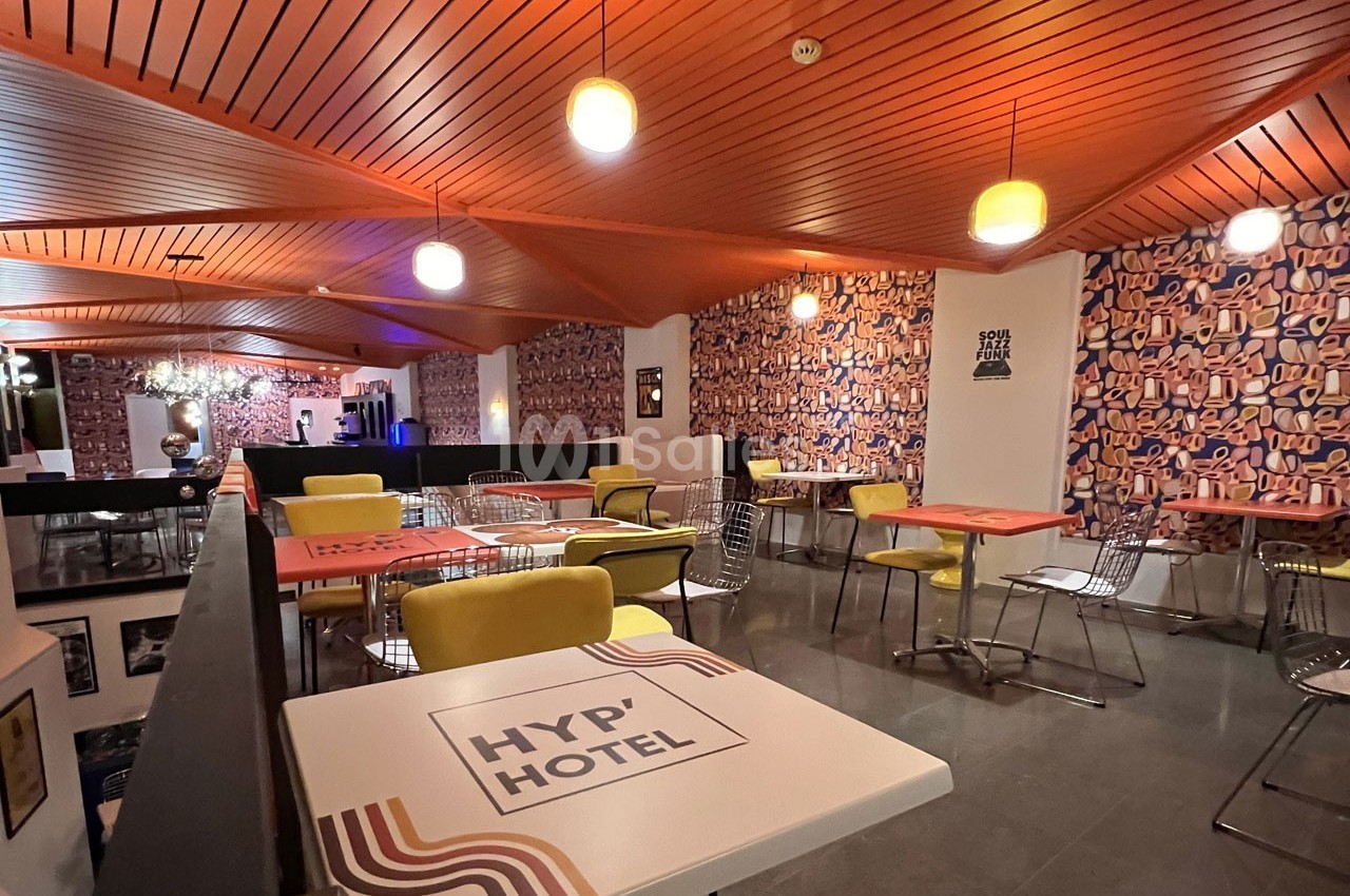 Salle de restaurant moderne avec tables colorées, chaises variées et murs décorés de motifs géométriques.