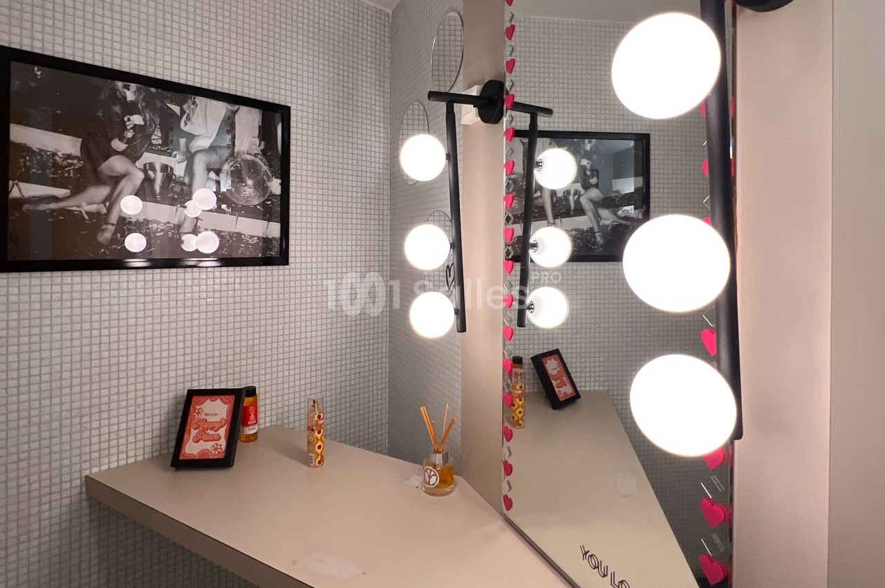 Miroir éclairé par des ampoules rondes dans une salle de bain au décor minimaliste avec cadre et accessoires.