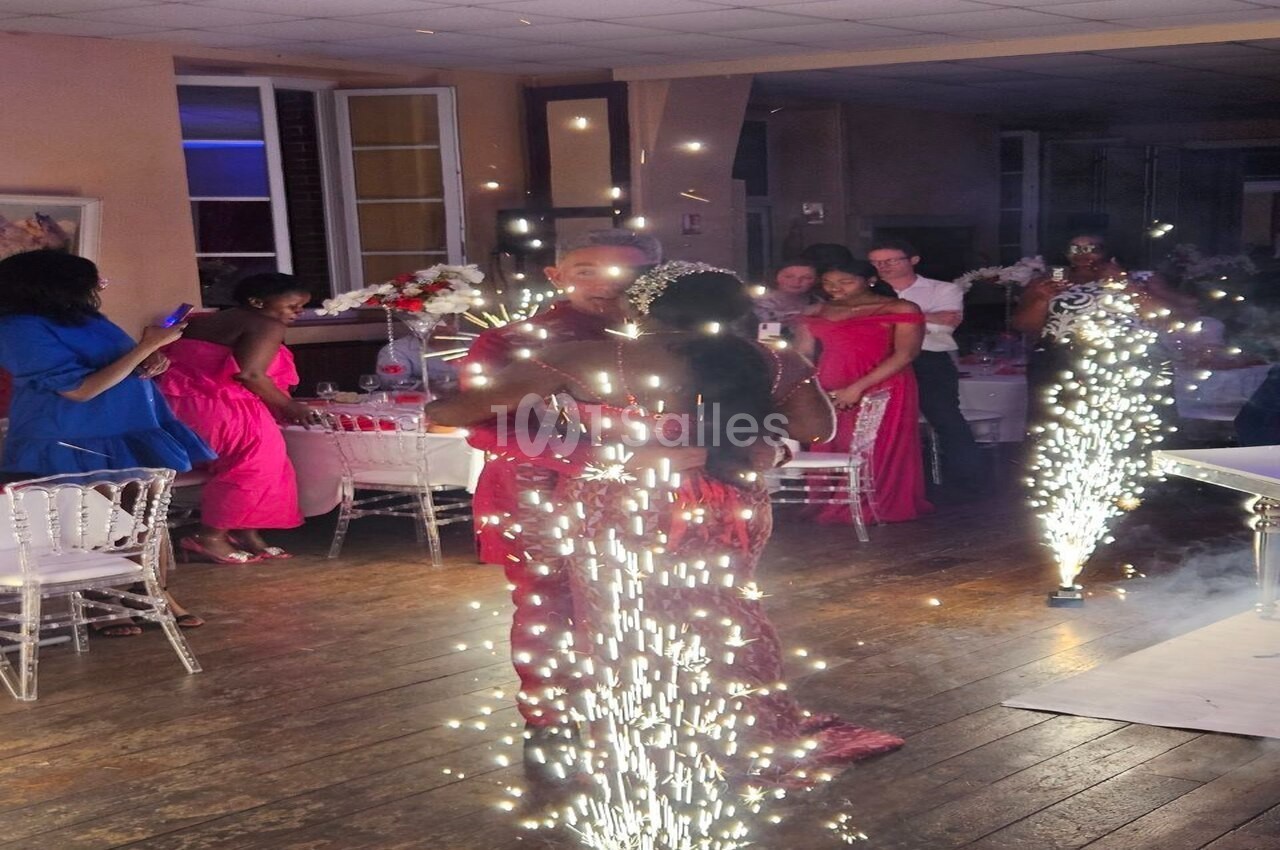 Des invités en tenue de soirée dansent au milieu de jets d'étincelles dans une salle décorée pour un événement.