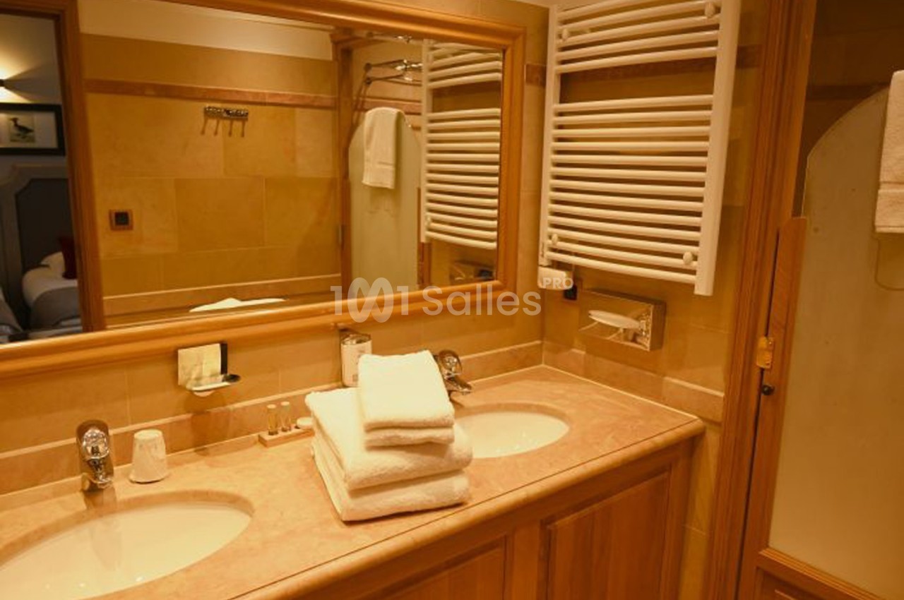 Salle de bain avec double vasque, miroir, serviettes pliées, radiateur mural et décor en tons beige.