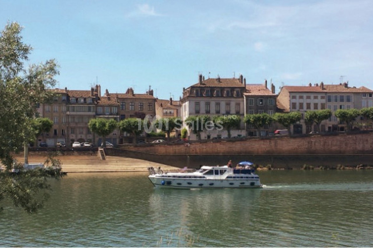 Bateau de plaisance naviguant sur une rivière bordée de maisons anciennes et d'arbres alignés.