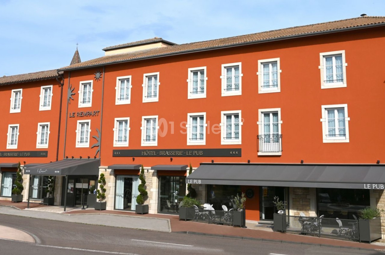 Façade d'un bâtiment rouge avec des fenêtres blanches, abritant un hôtel et une brasserie avec terrasses.