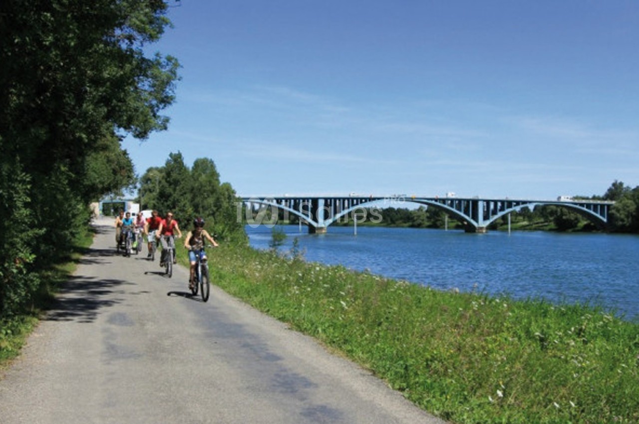 Un groupe de cyclistes roule sur une piste longeant une rivière avec un pont bleu visible à l'arrière-plan.